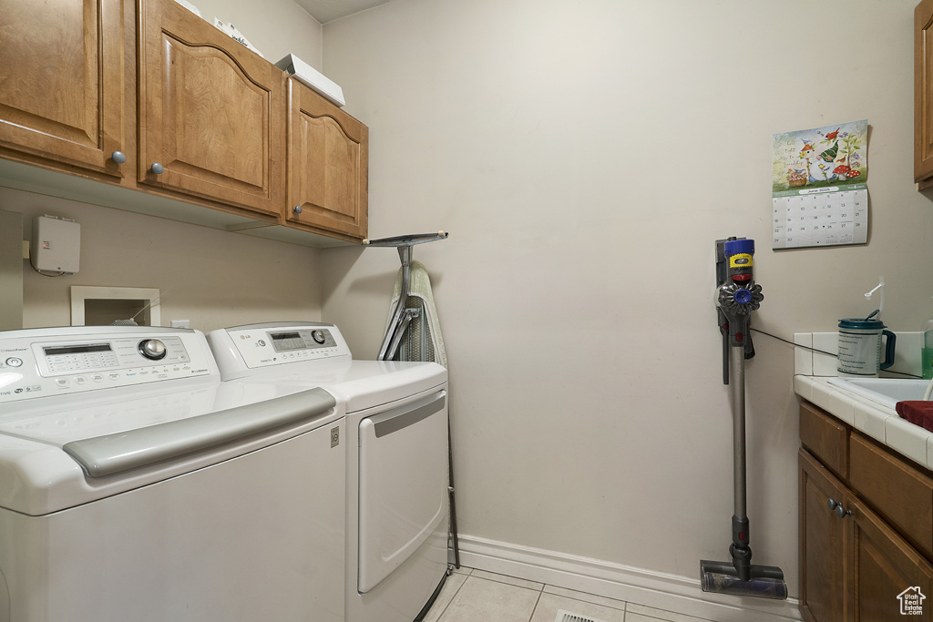 Laundry area featuring washing machine and dryer, cabinet space, and light tile patterned floors