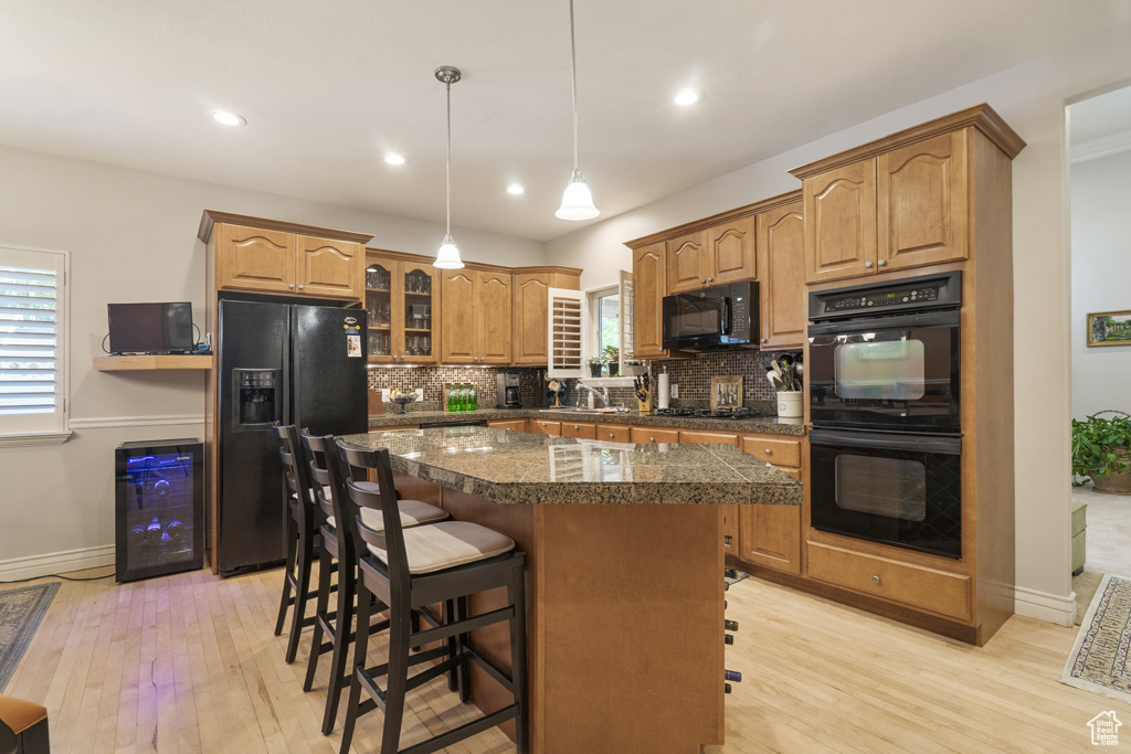 Kitchen with black appliances, wine cooler, light wood-style floors, tasteful backsplash, and recessed lighting
