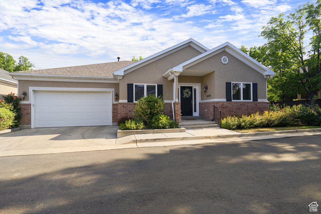 View of front of home with stucco siding, brick siding, an attached garage, and concrete driveway