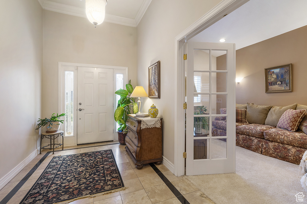 Entryway featuring inlaid floor details, ornamental molding, healthy amount of natural light, a high ceiling, and light tile patterned flooring