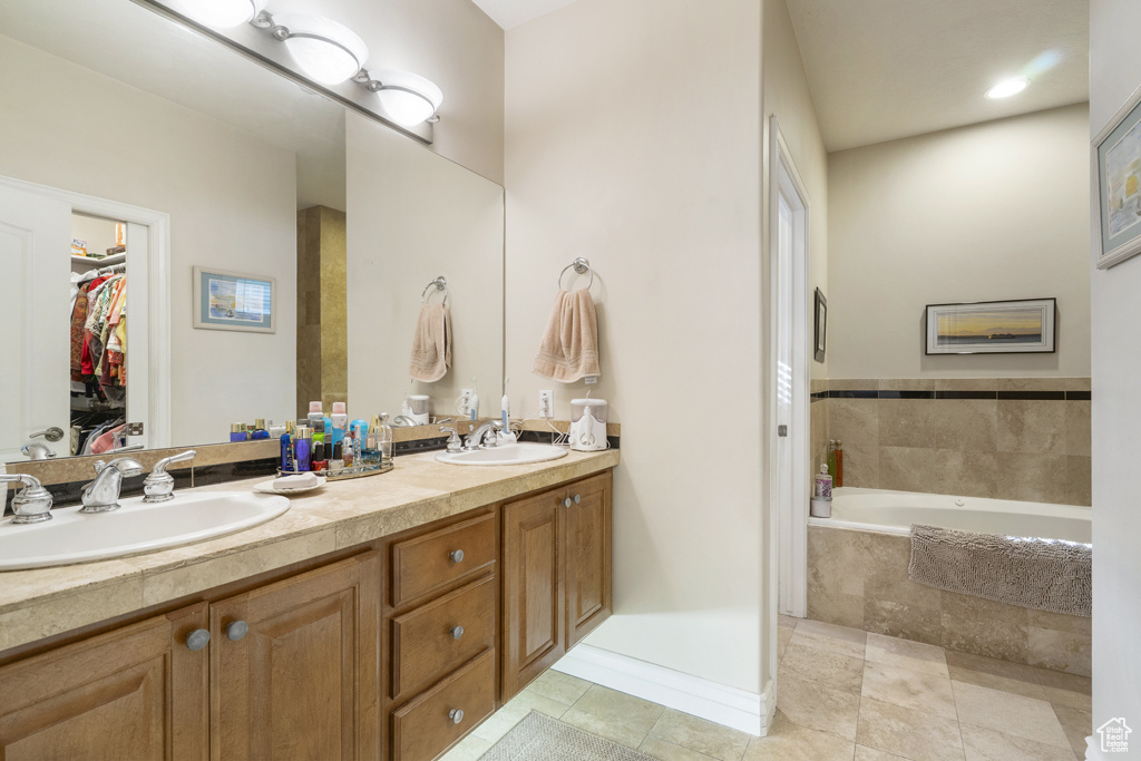 Full bath featuring double vanity, a relaxing tiled tub, tile patterned flooring, and a walk in closet
