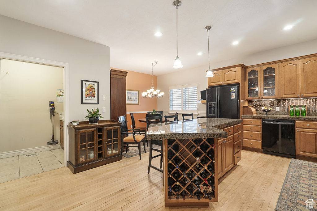 Kitchen featuring black appliances, glass insert cabinets, a breakfast bar, decorative backsplash, and light wood-style flooring