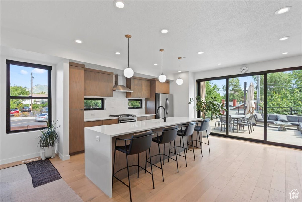 Kitchen featuring wall chimney range hood, modern cabinets, appliances with stainless steel finishes, light countertops, and light wood finished floors