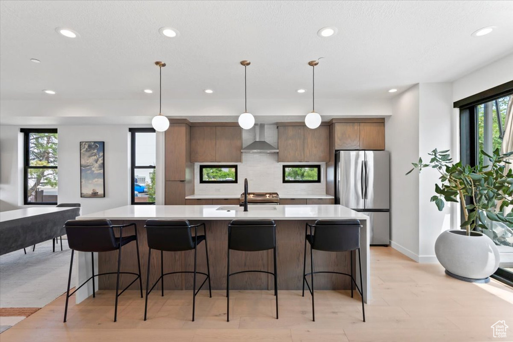 Kitchen featuring freestanding refrigerator, wall chimney exhaust hood, light countertops, recessed lighting, and decorative backsplash