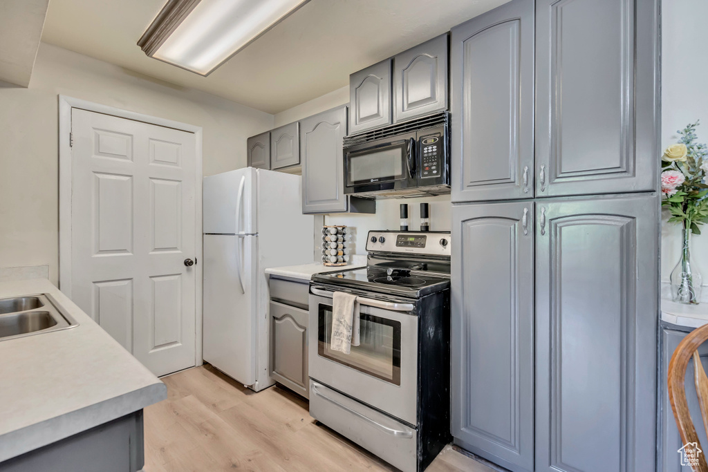 Kitchen featuring black microwave, stainless steel electric stove, gray cabinets, freestanding refrigerator, and light wood-style floors