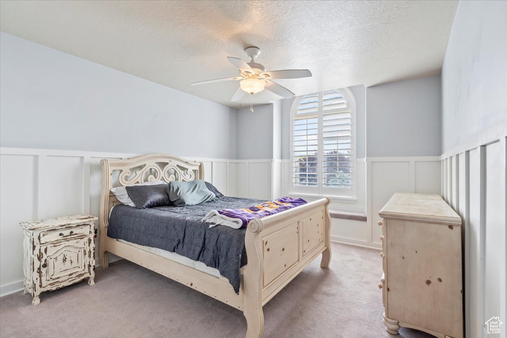 Bedroom with carpet, a decorative wall, a wainscoted wall, a textured ceiling, and a ceiling fan