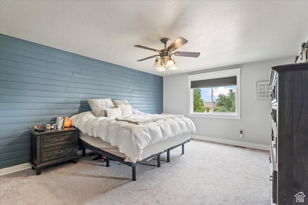 Bedroom featuring light carpet, a textured ceiling, ceiling fan, and wood walls