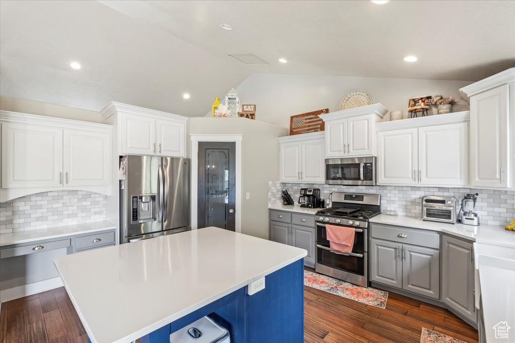 Kitchen with appliances with stainless steel finishes, vaulted ceiling, gray cabinets, a center island, and light countertops