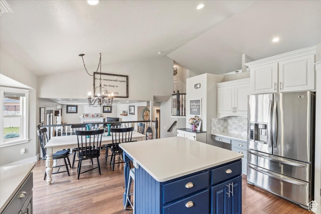 Kitchen featuring stainless steel fridge, blue cabinetry, vaulted ceiling, white cabinets, and decorative backsplash