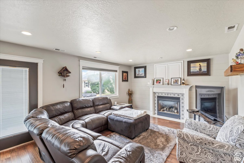 Living room featuring a tiled fireplace, a textured ceiling, wood finished floors, and recessed lighting