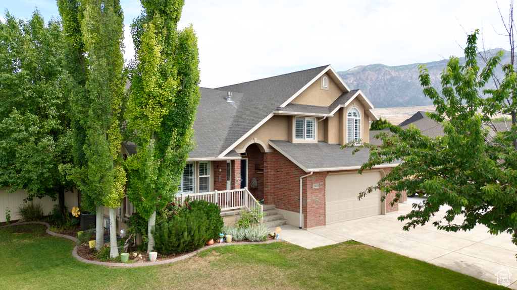 View of front of home with stucco siding, concrete driveway, brick siding, covered porch, and a front lawn