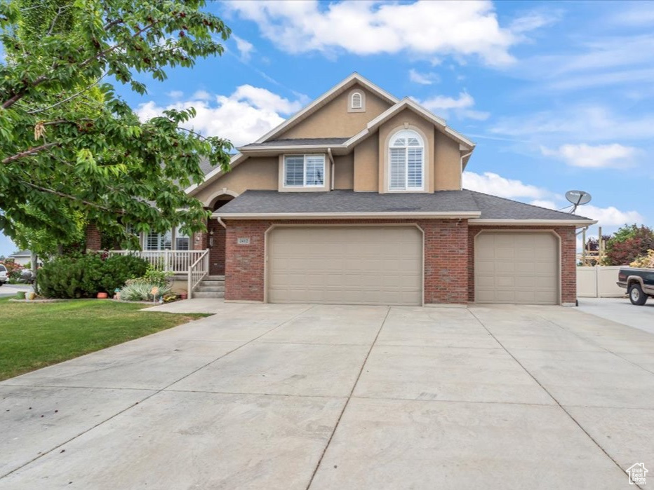 Traditional home with concrete driveway, an attached garage, brick siding, stucco siding, and a front lawn