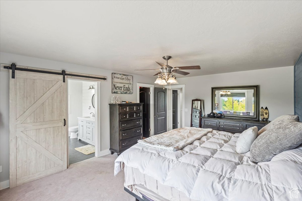 Bedroom featuring a barn door, carpet flooring, ensuite bathroom, and a ceiling fan