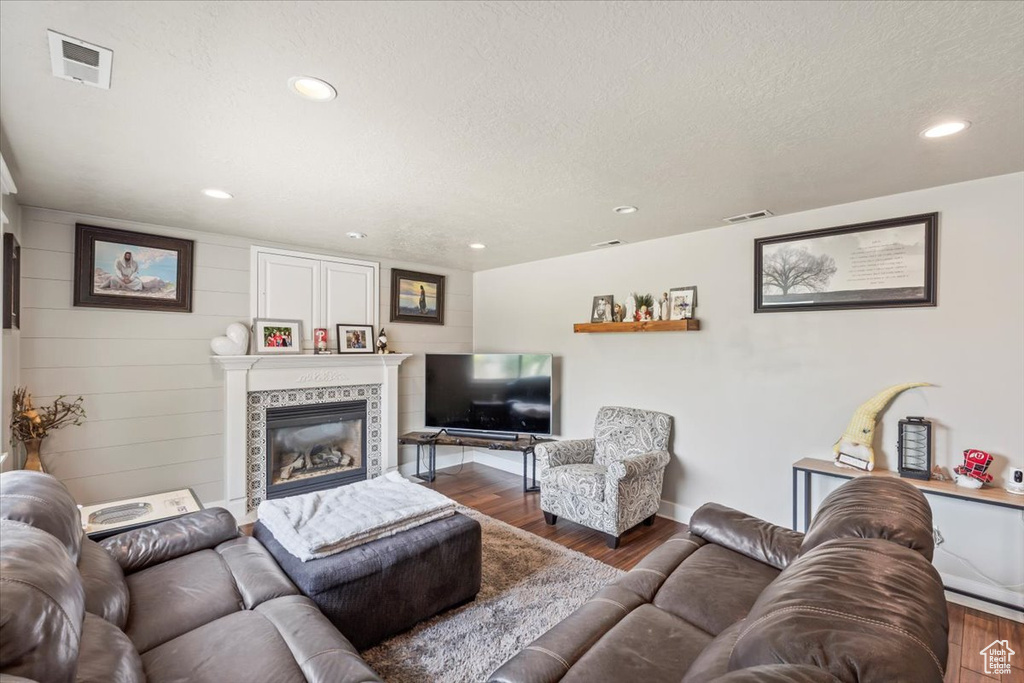 Living area with wood finished floors, a tiled fireplace, recessed lighting, and a textured ceiling