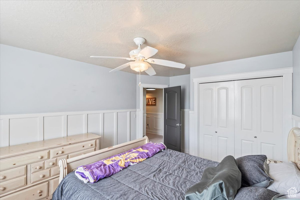 Bedroom featuring a closet, a wainscoted wall, a decorative wall, ceiling fan, and a textured ceiling