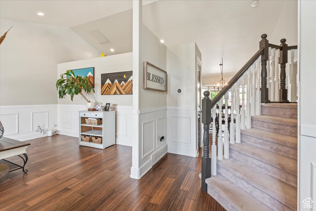 Entrance foyer with wainscoting, wood finished floors, stairs, a decorative wall, and a chandelier