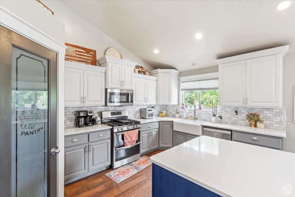 Kitchen featuring stainless steel appliances, gray cabinets, decorative backsplash, wood finished floors, and vaulted ceiling