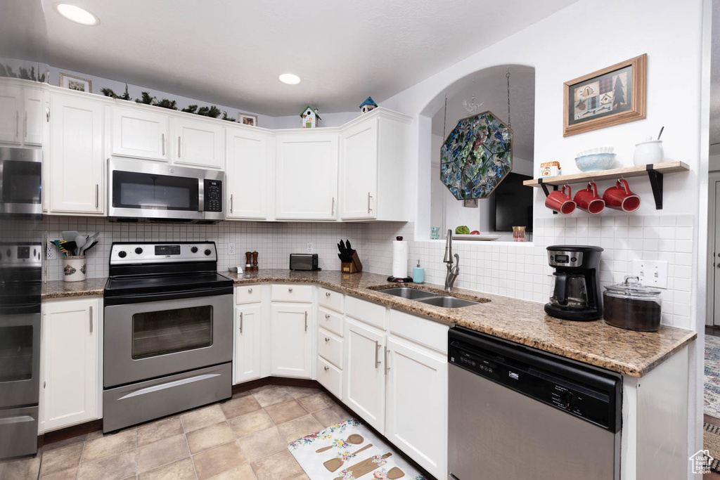 Kitchen with stainless steel appliances, white cabinets, decorative backsplash, and light stone counters