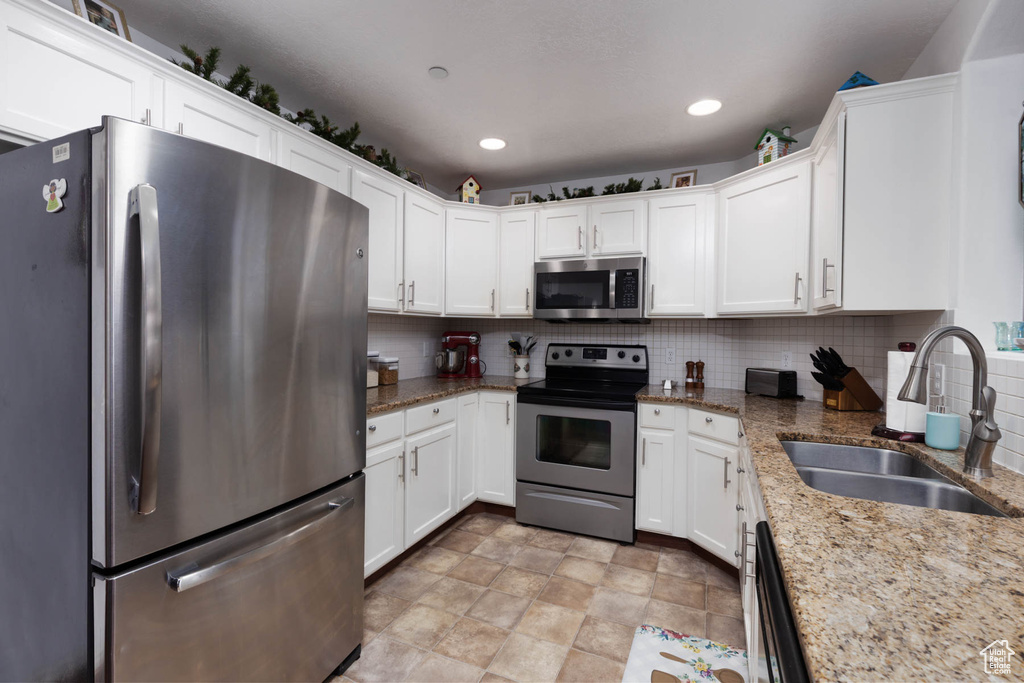 Kitchen with stainless steel appliances, white cabinets, tasteful backsplash, recessed lighting, and light stone counters