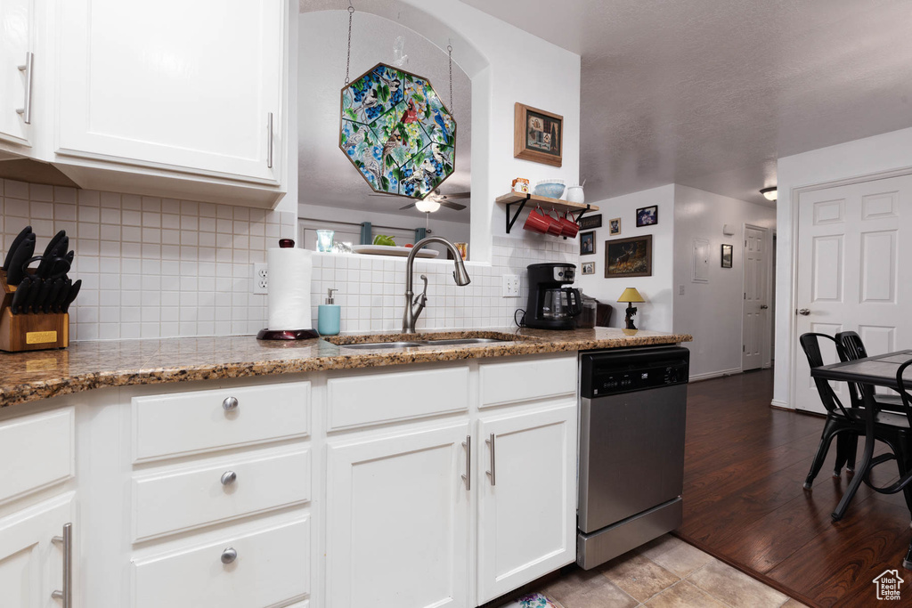 Kitchen with stainless steel dishwasher, decorative backsplash, white cabinetry, and stone countertops