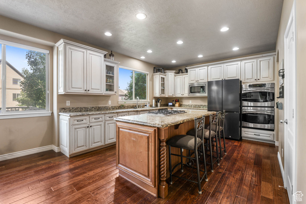 Kitchen featuring stainless steel appliances, glass insert cabinets, a kitchen island, a kitchen bar, and white cabinetry