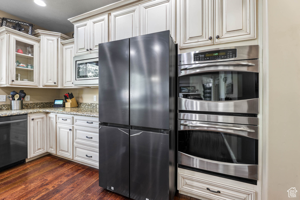 Kitchen with freestanding refrigerator, stainless steel double oven, dishwasher, light stone countertops, and dark wood-style floors