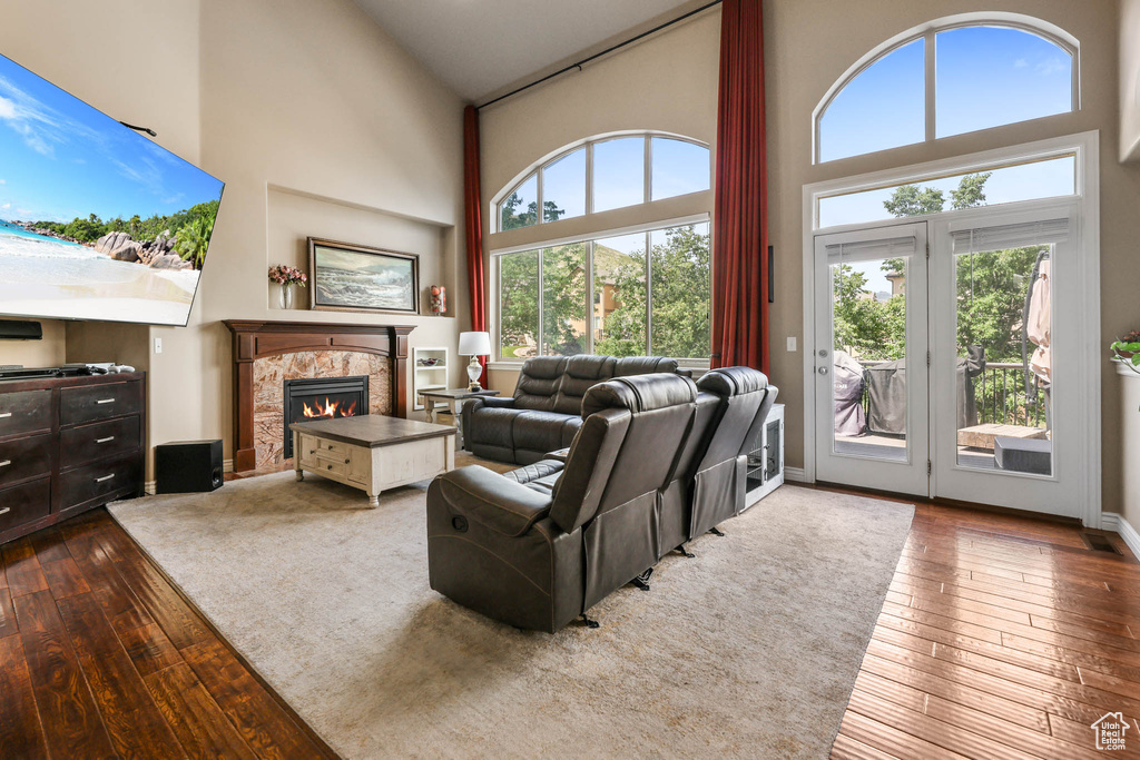 Living room with high vaulted ceiling, dark wood-type flooring, healthy amount of natural light, and a tiled fireplace