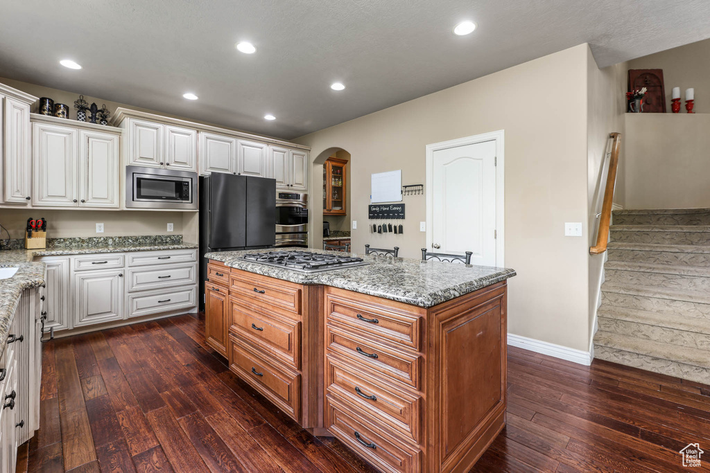 Kitchen with appliances with stainless steel finishes, dark wood finished floors, arched walkways, a kitchen island, and light stone countertops