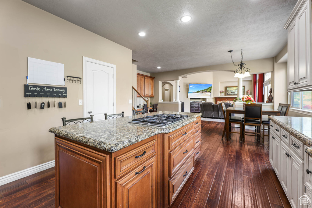 Kitchen with arched walkways, stainless steel gas stovetop, decorative columns, dark wood finished floors, and recessed lighting