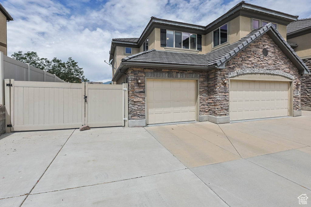 View of home\'s exterior featuring stone siding, a gate, driveway, stucco siding, and an attached garage