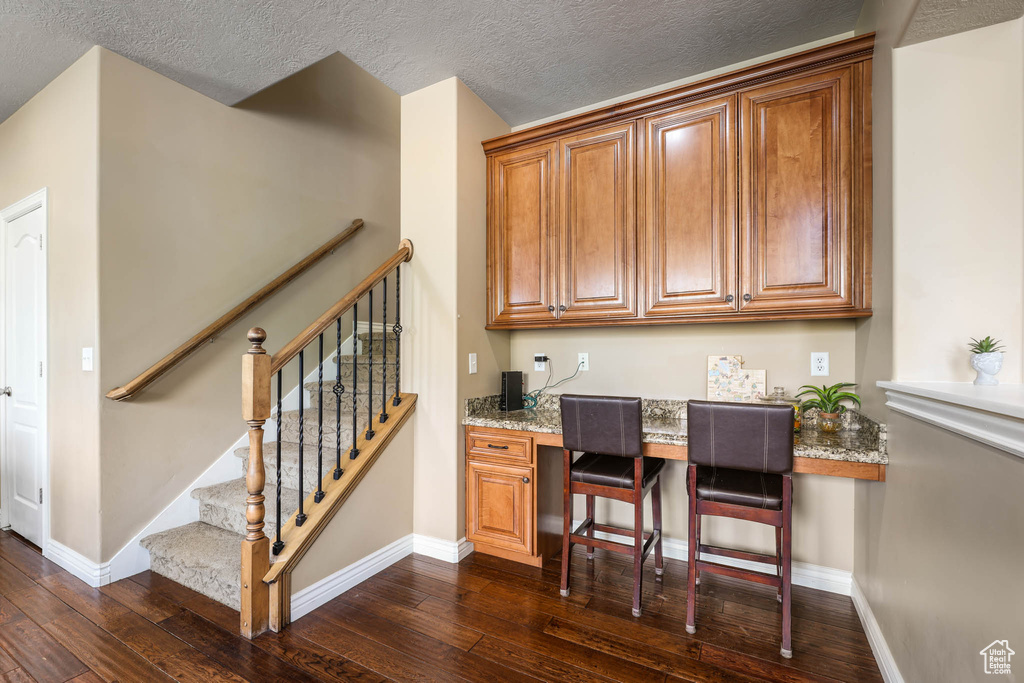 Bar area with dark wood-style floors, stairway, a textured ceiling, and built in desk