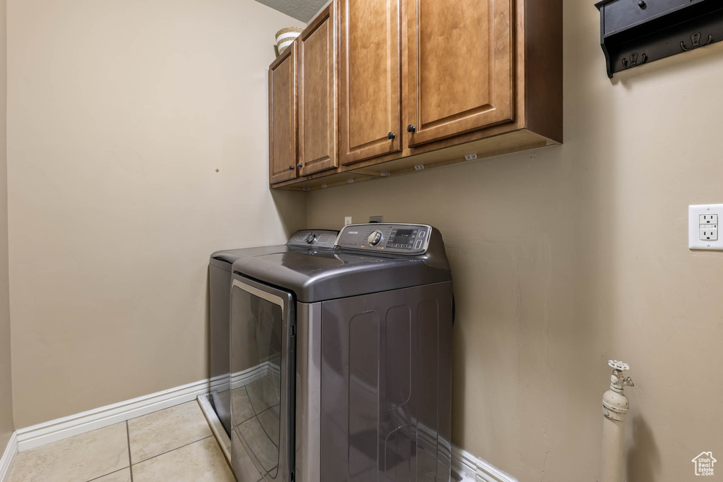 Washroom with washing machine and dryer, cabinet space, and light tile patterned flooring