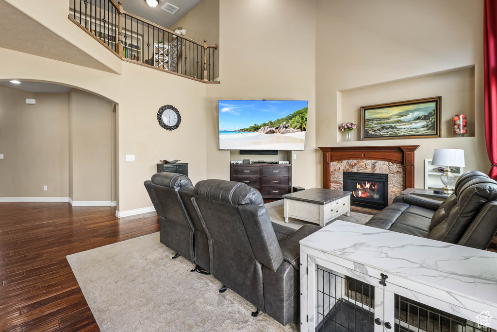 Living room featuring arched walkways, a stone fireplace, wood finished floors, and a high ceiling