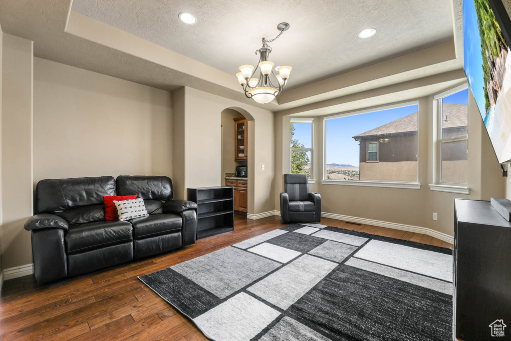 Living room featuring arched walkways, a tray ceiling, hardwood / wood-style flooring, a chandelier, and a textured ceiling