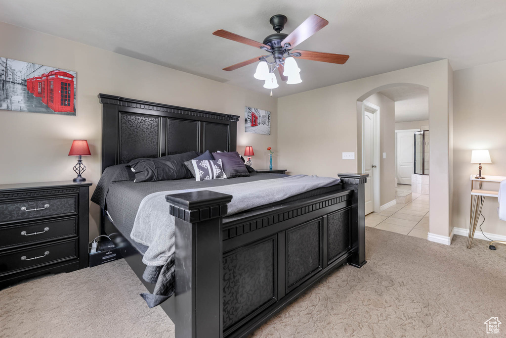Bedroom with arched walkways, light carpet, ceiling fan, and light tile patterned floors