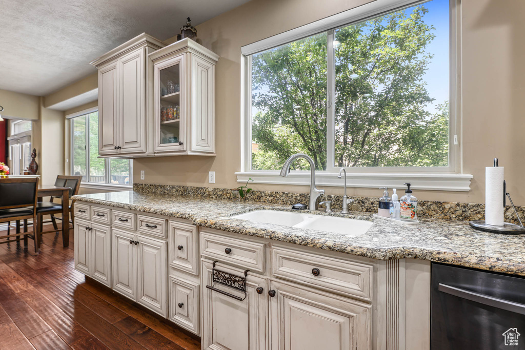 Kitchen featuring stainless steel dishwasher, dark wood-type flooring, glass insert cabinets, and light stone counters