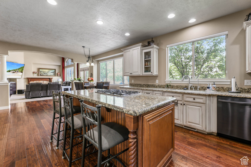 Kitchen featuring stainless steel appliances, a textured ceiling, light stone countertops, glass insert cabinets, and a breakfast bar