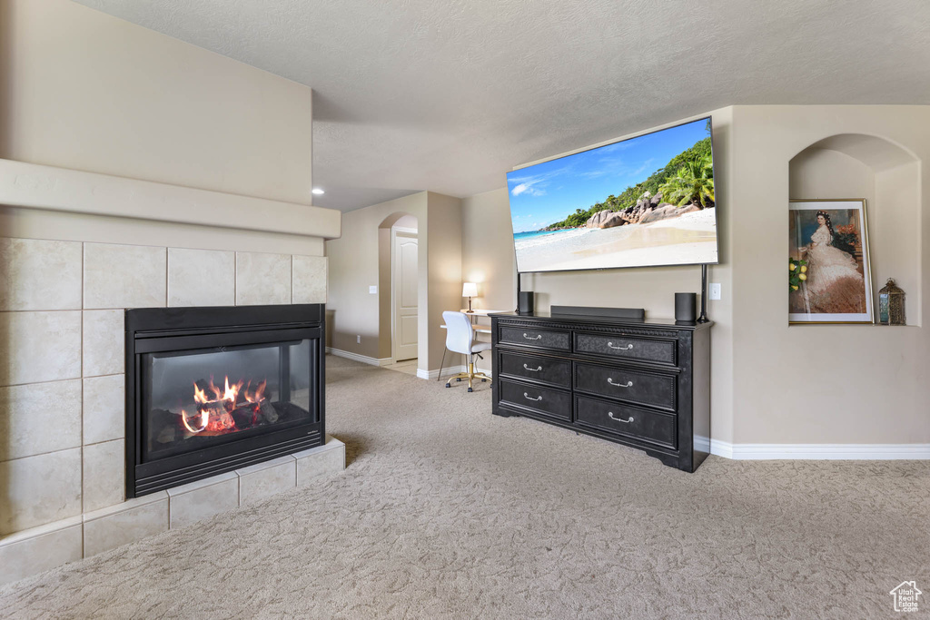 Carpeted living room featuring a tile fireplace, arched walkways, and a textured ceiling