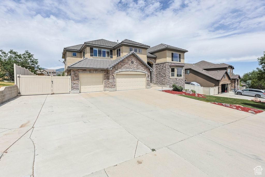 View of front of home featuring stone siding, concrete driveway, stucco siding, a gate, and a garage