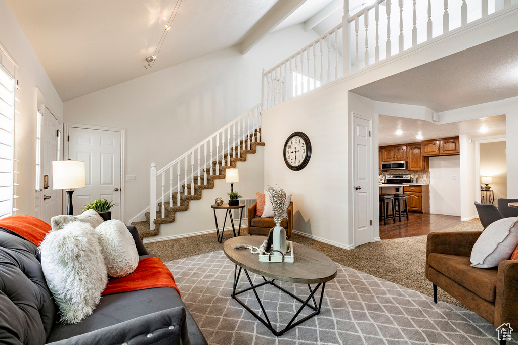 Carpeted living room with stairs and high vaulted ceiling