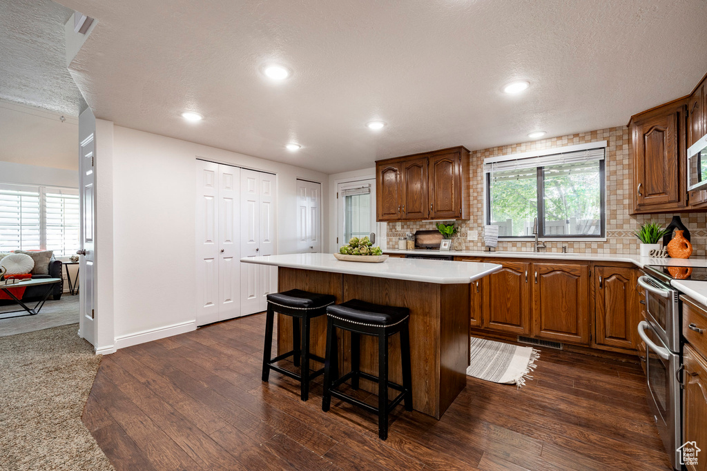 Kitchen featuring appliances with stainless steel finishes, dark wood-type flooring, decorative backsplash, a center island, and a textured ceiling