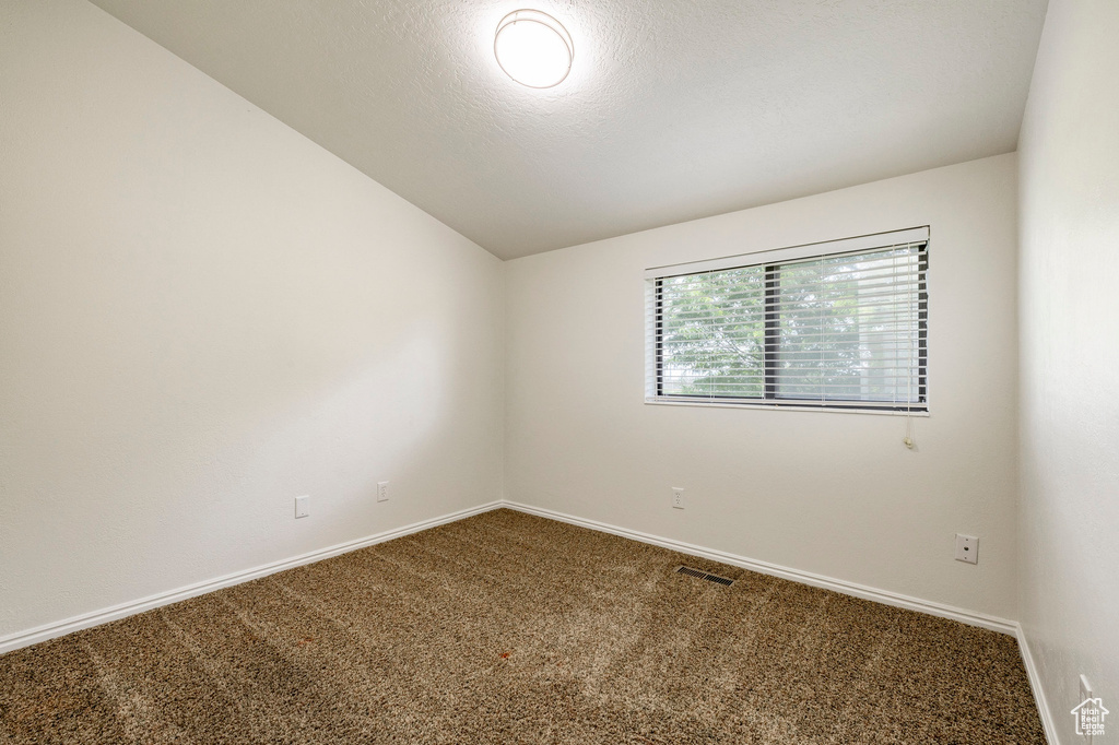 Carpeted empty room featuring lofted ceiling and baseboards
