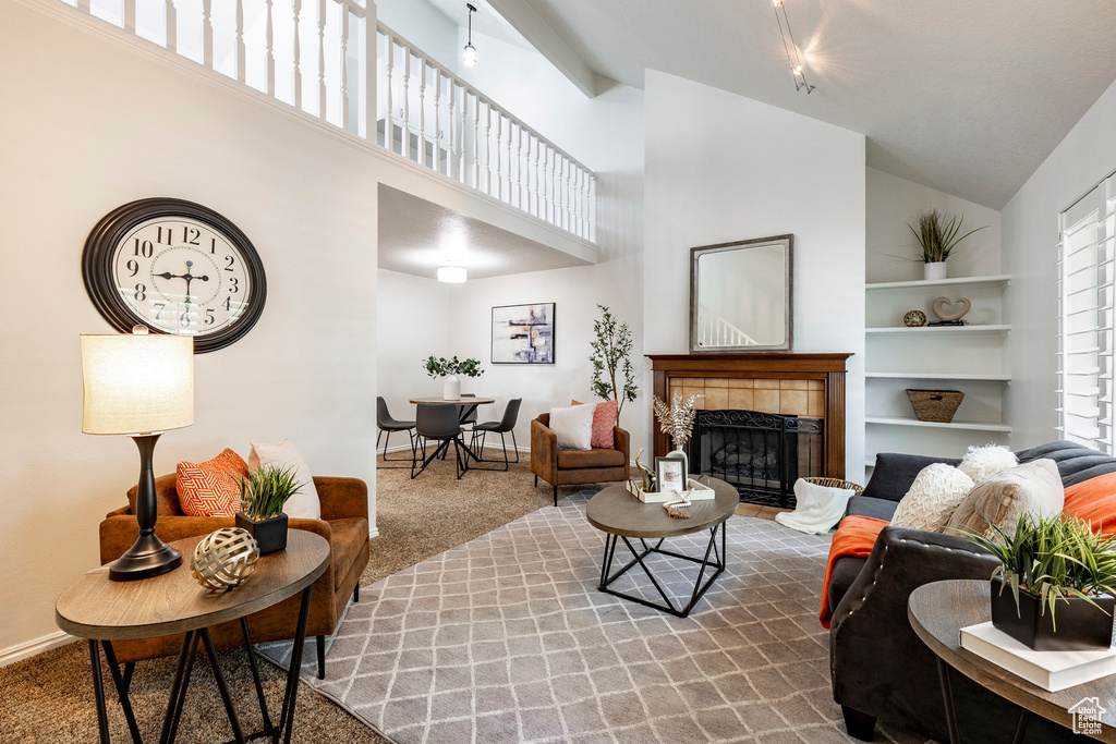 Living area with carpet flooring, a tile fireplace, high vaulted ceiling, and built in shelves