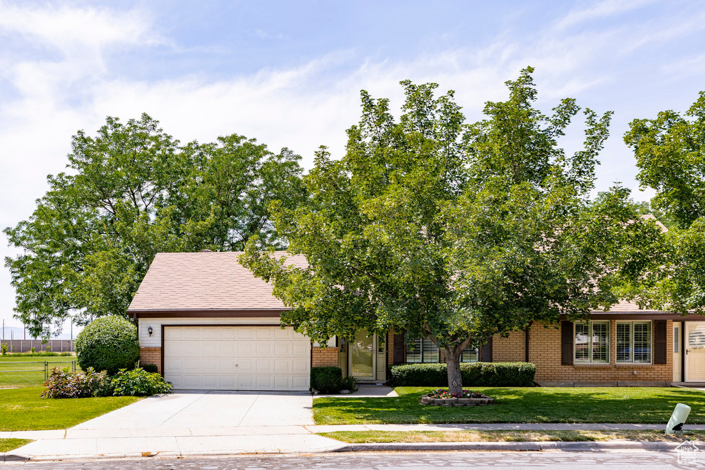 Obstructed view of property with brick siding, an attached garage, concrete driveway, and a front yard