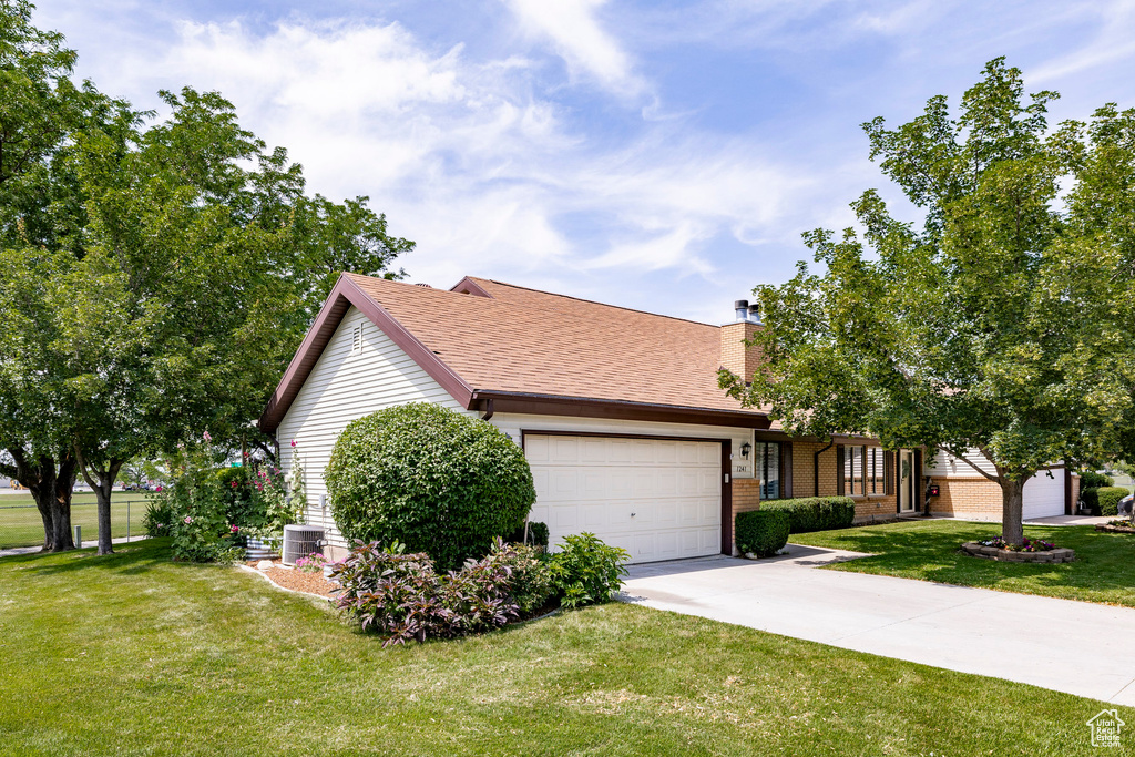 View of front of home with a garage, concrete driveway, a front lawn, a chimney, and brick siding