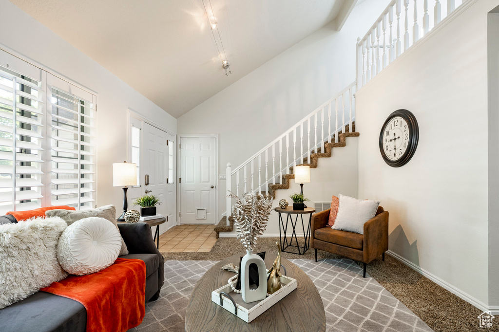 Carpeted living area featuring healthy amount of natural light, stairs, and high vaulted ceiling