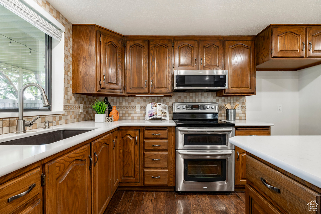 Kitchen featuring appliances with stainless steel finishes, light countertops, brown cabinetry, dark wood finished floors, and backsplash