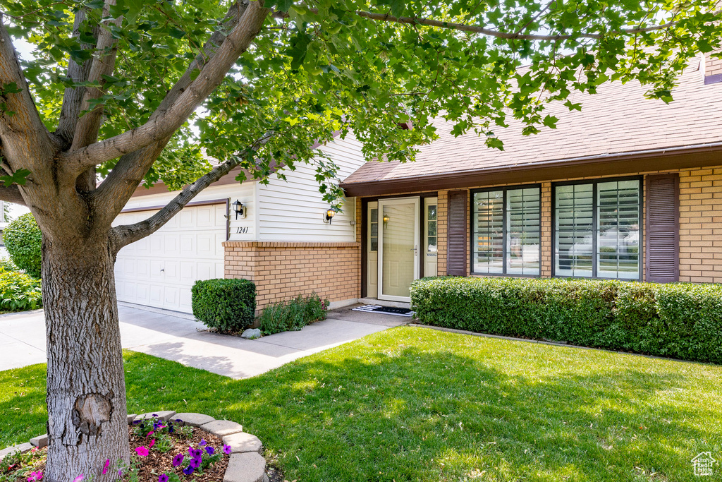 View of front of home featuring brick siding, a front yard, and a garage