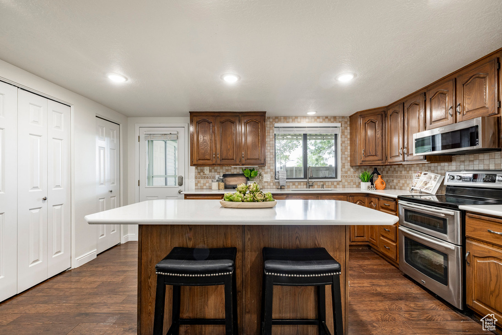 Kitchen with appliances with stainless steel finishes, light countertops, tasteful backsplash, a kitchen breakfast bar, and recessed lighting