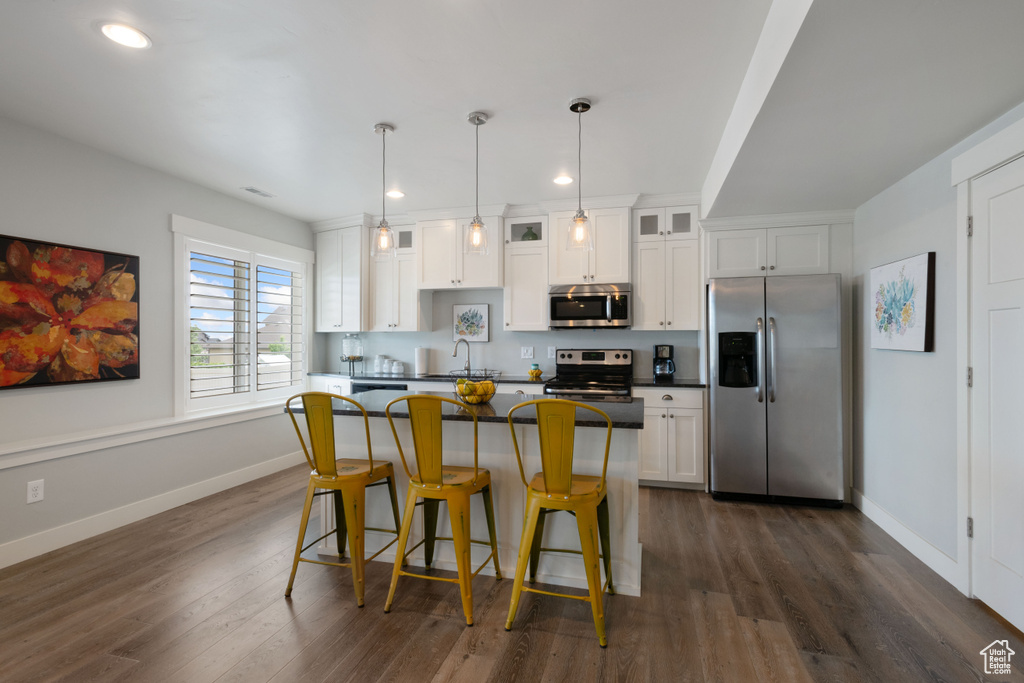 Kitchen with stainless steel appliances, white cabinetry, a breakfast bar, dark wood-type flooring, and recessed lighting